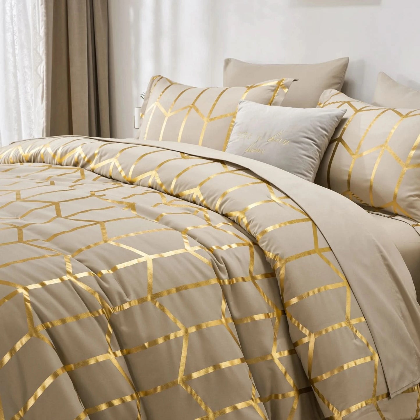 Beige and gold patterned bedding set on a bed with white curtains in the background.